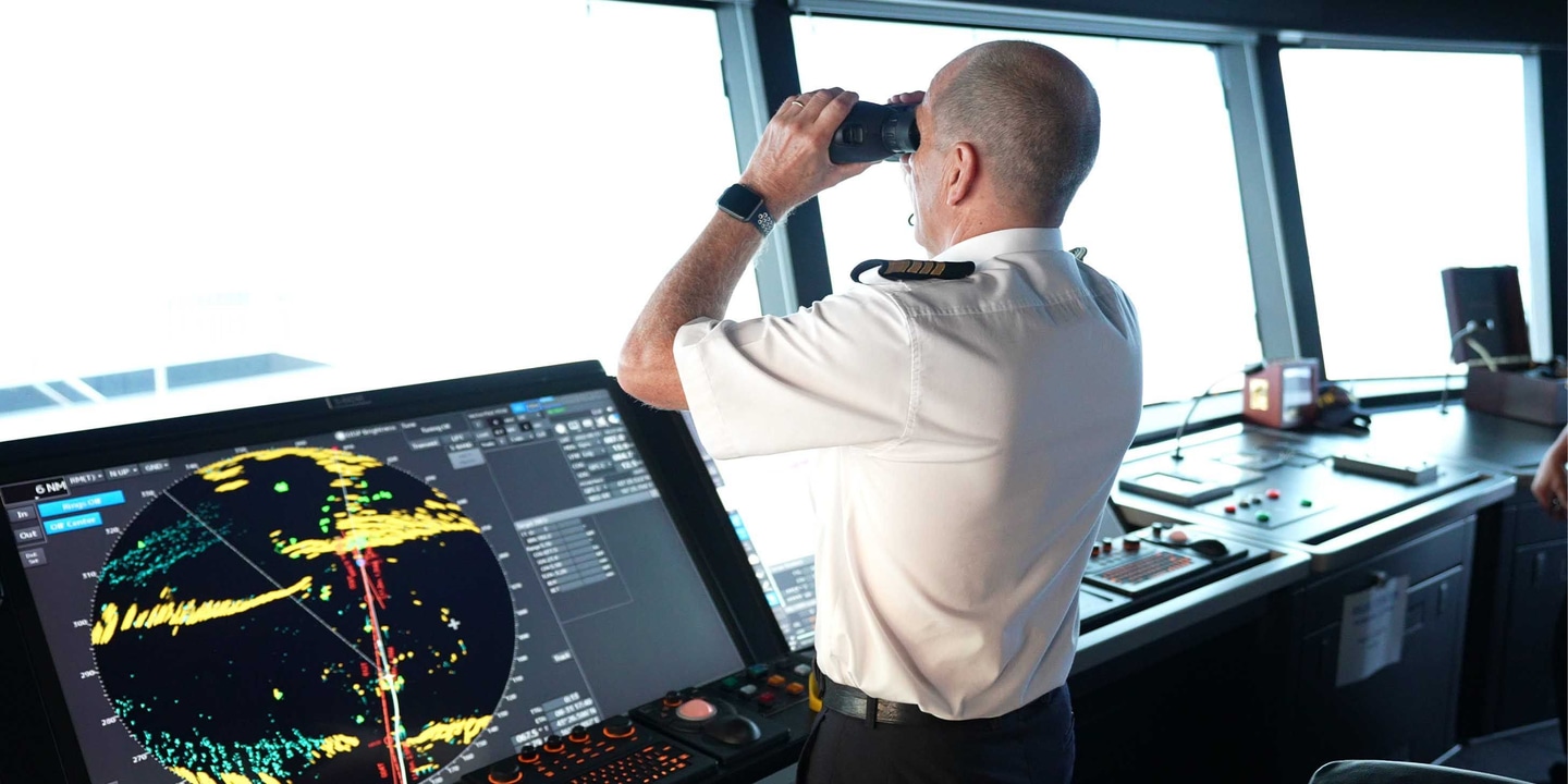 Captain looking out of binoculars towards the horizon from the navigation bridge of an Emerald Cruises luxury yacht cruise