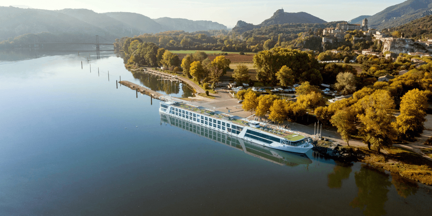 Emerald Ship can be seen docked by a bank. The trees in the background are a mix of green and yellow.