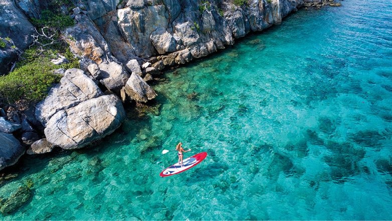 Aerial view of a woman enjoying paddleboarding on the clear blue waters of the Caribbean Sea along the rocky coastline