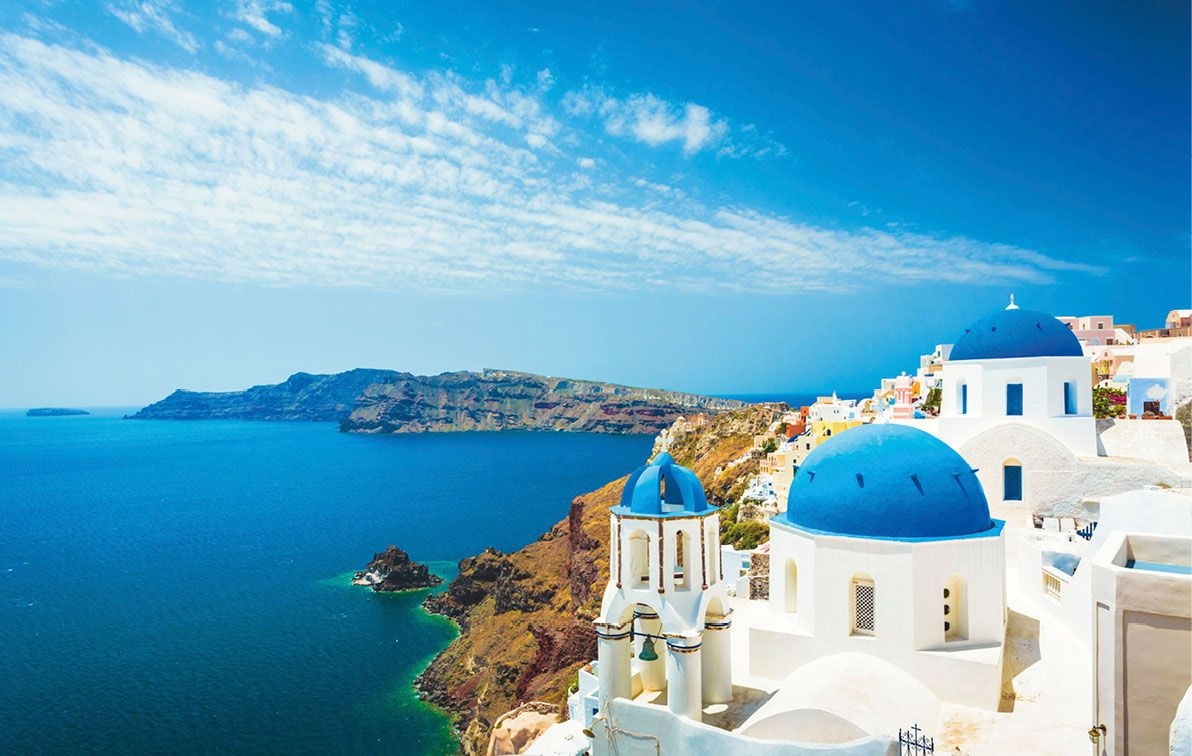 Blue-domed church of Santorini, Greece on a bright sunny day, with light cloudy sky and deep blue sea