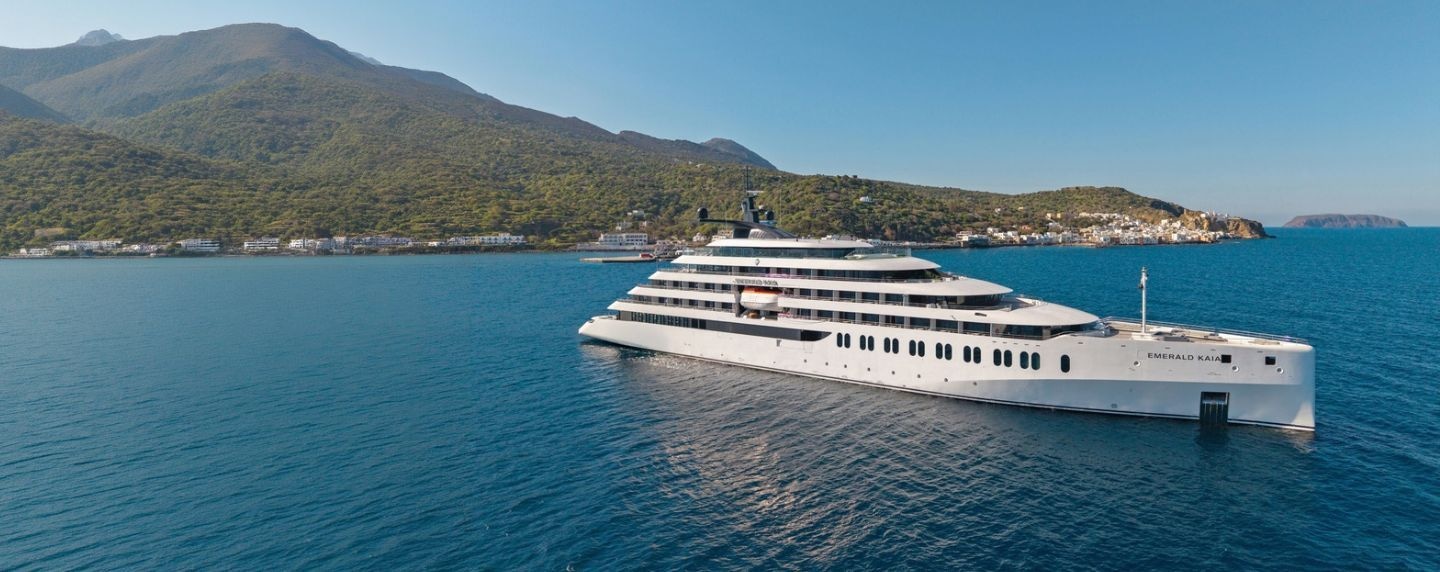 Emerald Kaia exterior in deep blue waters near a coastal mountain landscape.
